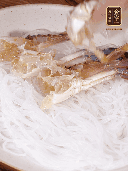 盤底墊上粉絲，擺上梭子蟹、火腿片，撒姜粒，淋上蒸魚豉油、花雕酒調(diào)味腌制15分鐘